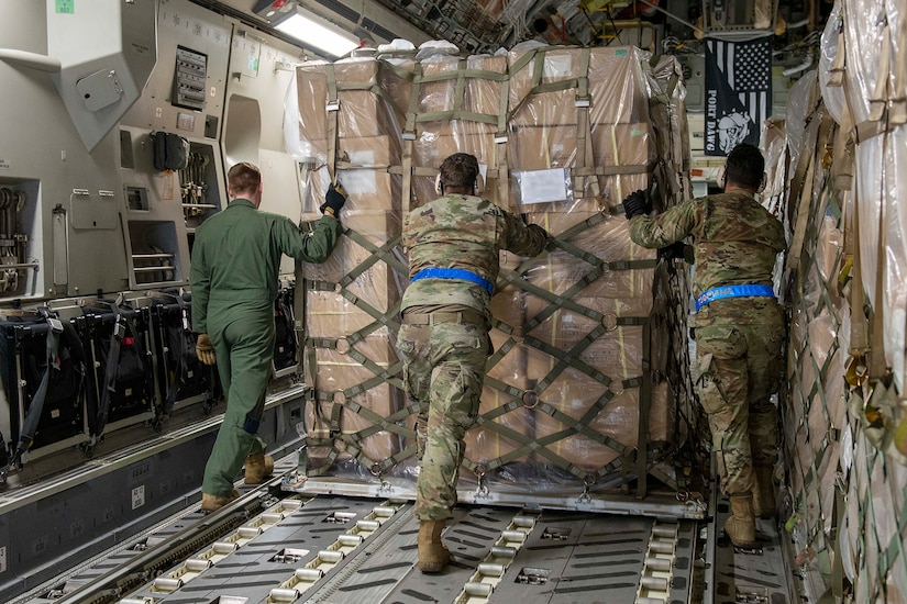 Service members push cargo into the back of a plane.