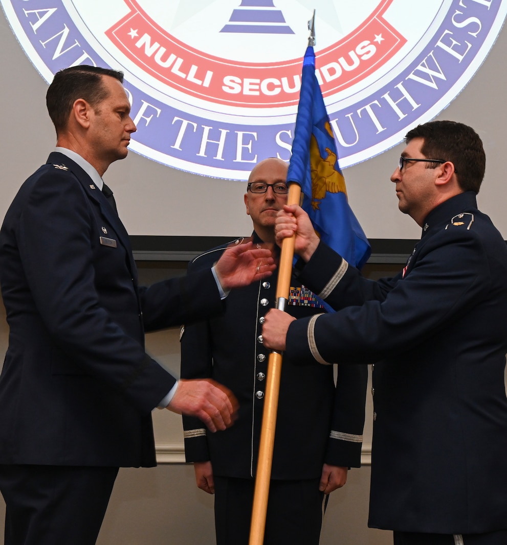 Male Air Force officers pass a flag between them with one male enlisted standing in the background seen between them.