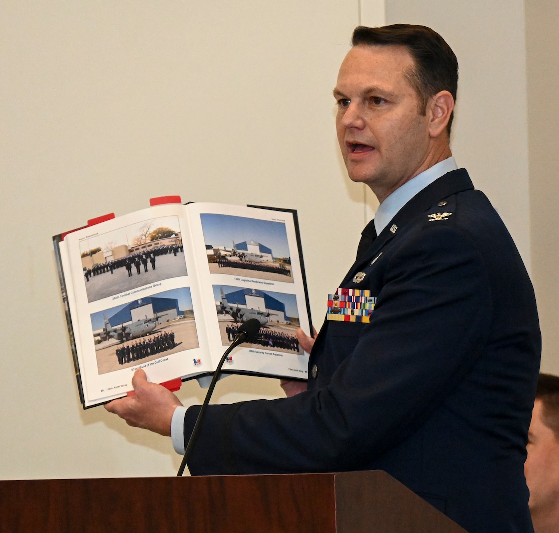Male Air Force officer holds open a book while standing behind a podium.