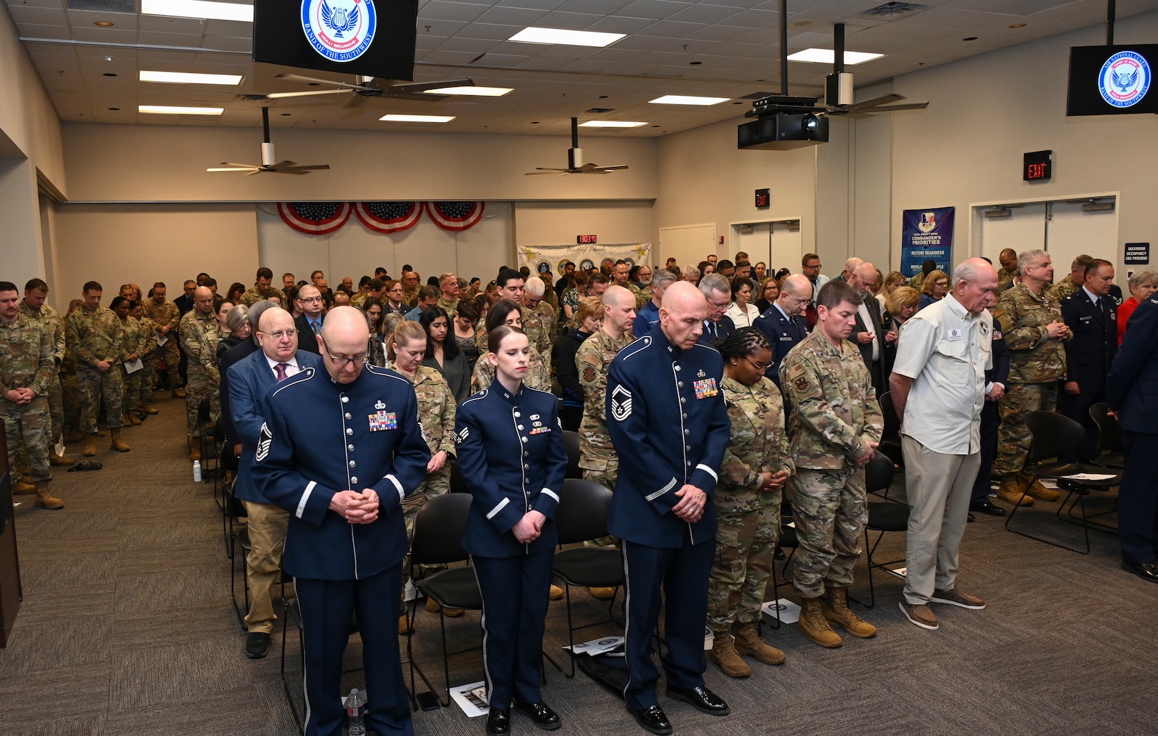 Overhead shot of standing Air Force members attending an indoors ceremony.