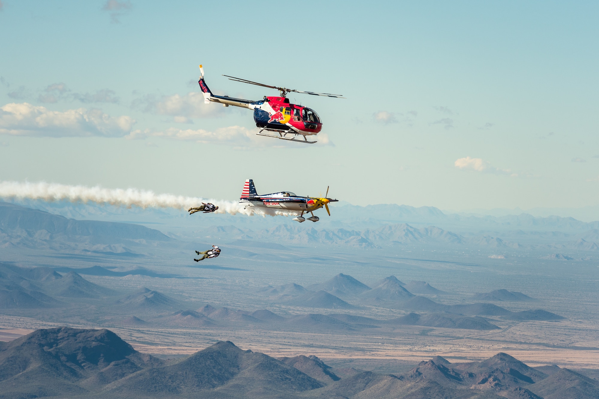 A plane and helicopter fly as two men skydive.