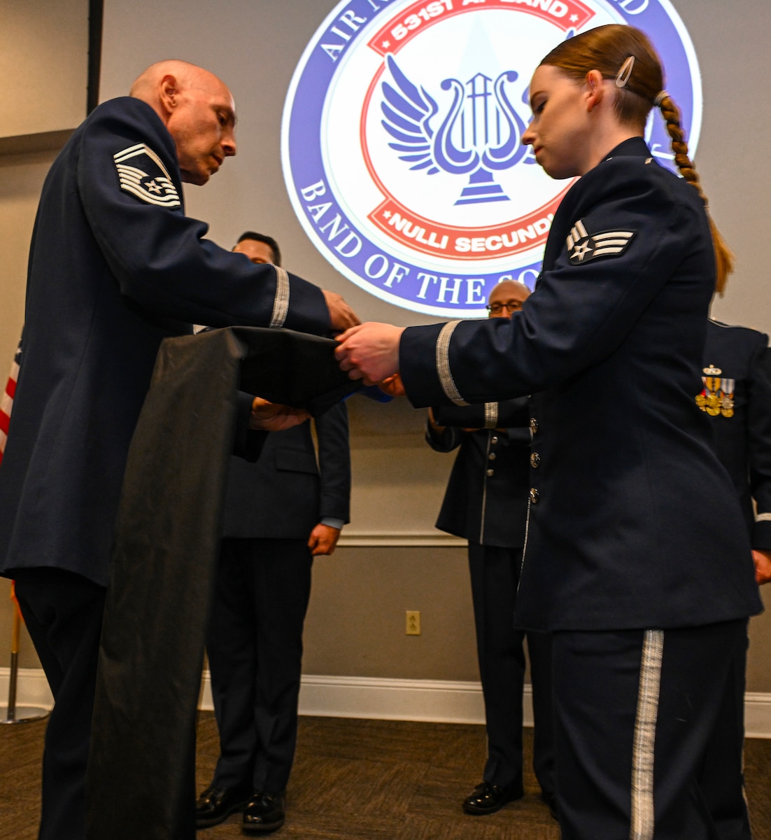 Air Force male slides a sheath over a flag while an Air Force female holds flag pole.