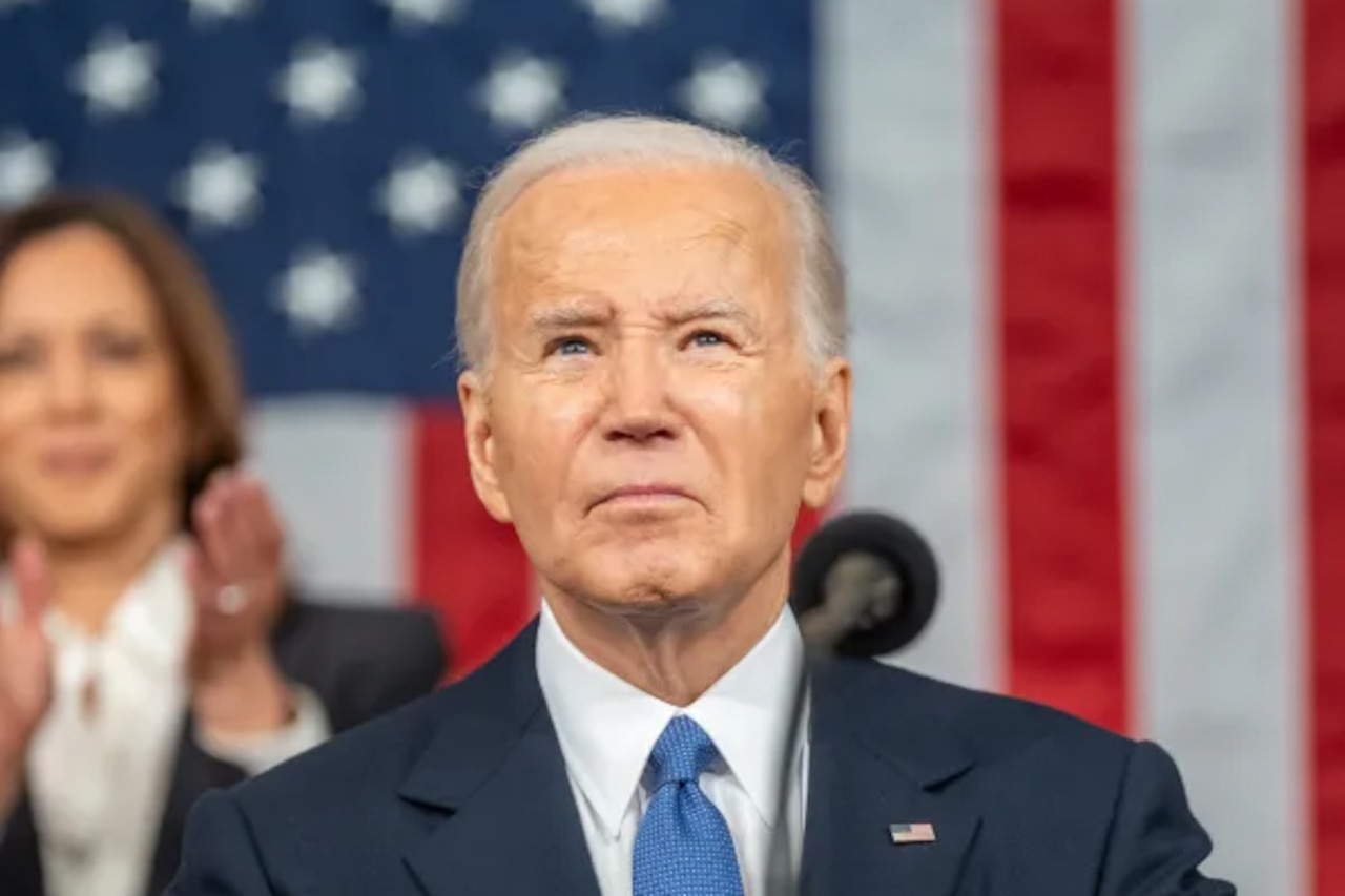 President Joe Biden stands at a lectern in front of a U.S. flag and Vice President Kamala Harris applauds behind him.