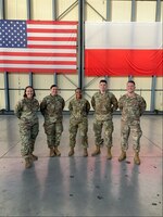 Soldiers stand in front of the American and Polish flags