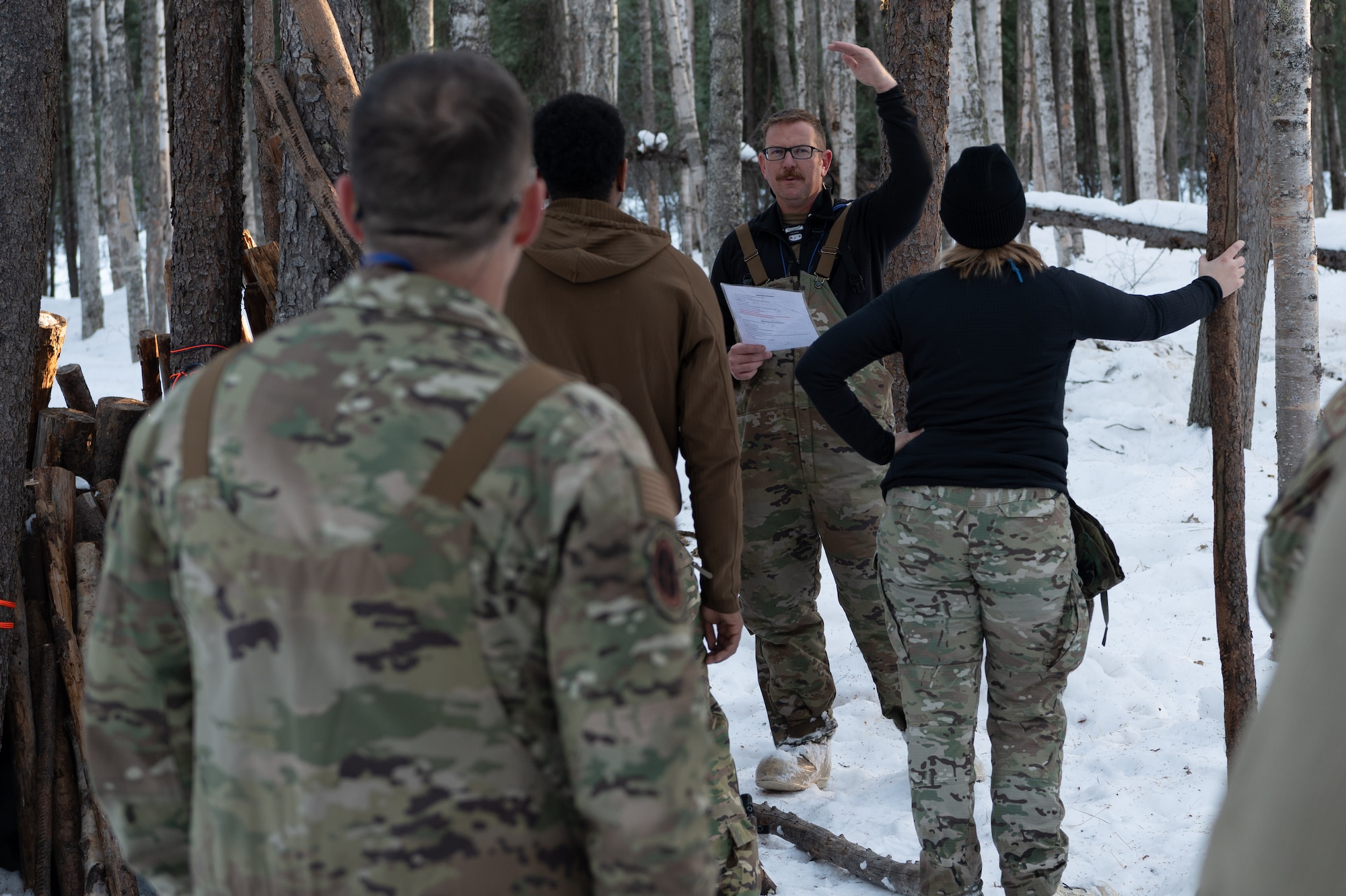 Arctic survival students of class 24-09, element one, go over instructions for A-frame shelter construction at the Arctic field training area on Eielson Air Force Base, Feb. 14, 2024.