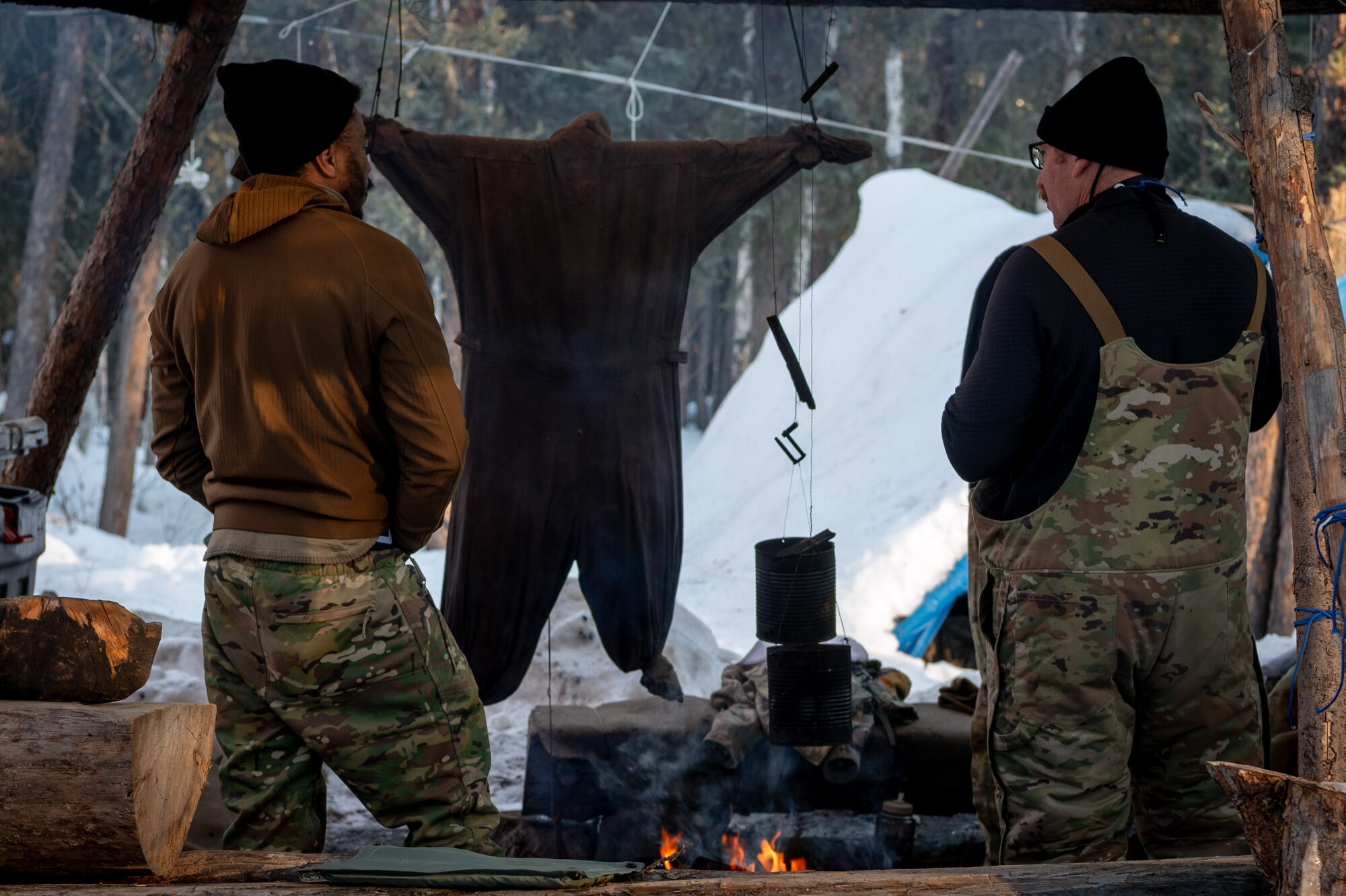 U.S. Air Force Staff Sgt. Samuel Wells (left) and Master Sgt. James Cain, Arctic survival students of class 24-09, element one, stand by a campfire at the Arctic field training area on Eielson Air Force Base, Feb. 14, 2024.