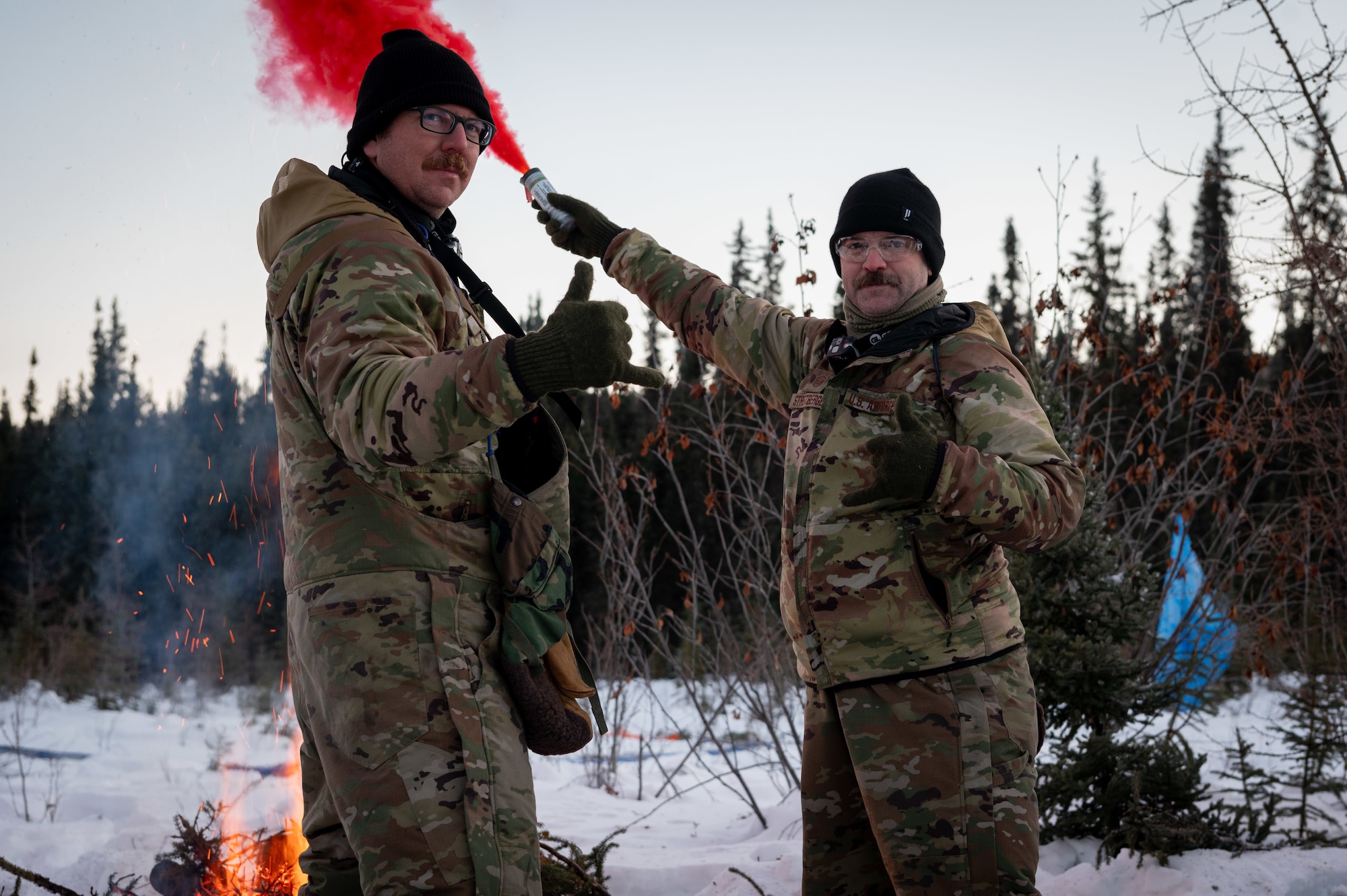 U.S. Air Force Master Sgt. James Cain (left) and Master Sgt. Justin Streitberger give the shaka gesture as they use MK-124 signaling flares at their ground-to-air signal (GTAS) area in the Arctic field training area on Eielson Air Force Base, Feb. 16, 2024.