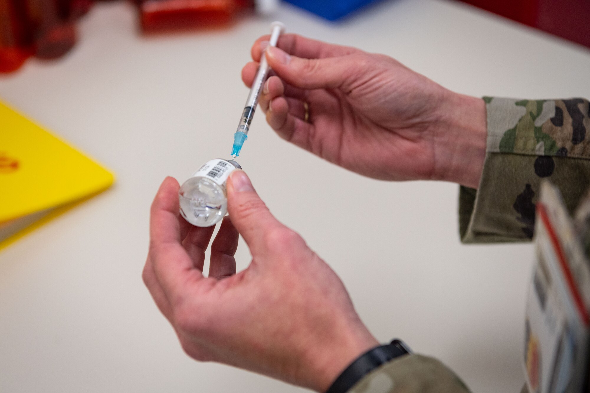 Person drawing liquid out vial with a syringe.