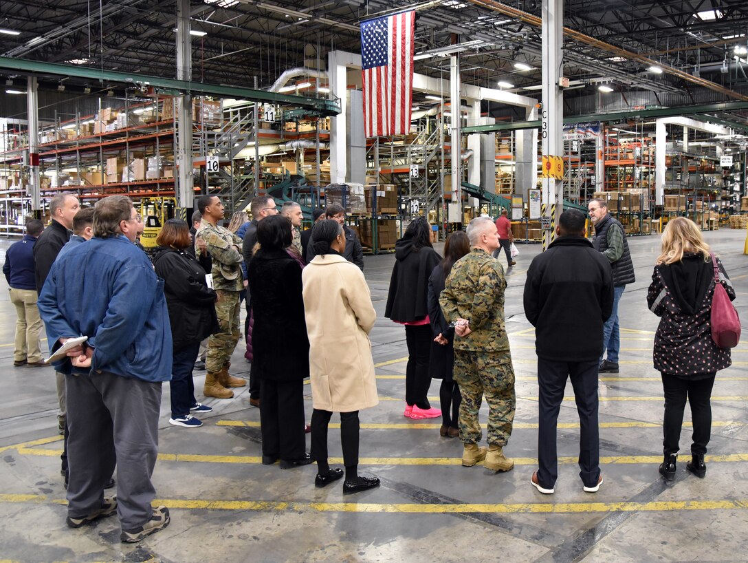 Photo is of a large group of people standing in a big warehouse.