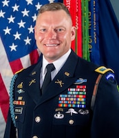 Soldier in dress uniform with US Flag and Army flag in the background