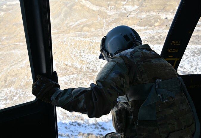Flight engineer leans out the door of a hovering UH-1N