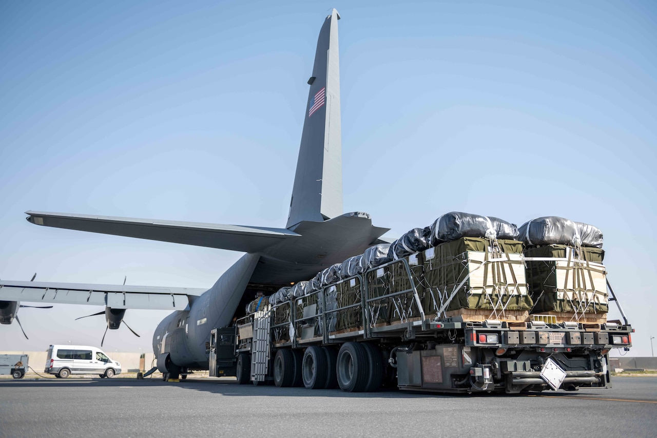 Pallets of humanitarian aid are staged at the ramp of a military cargo plane.