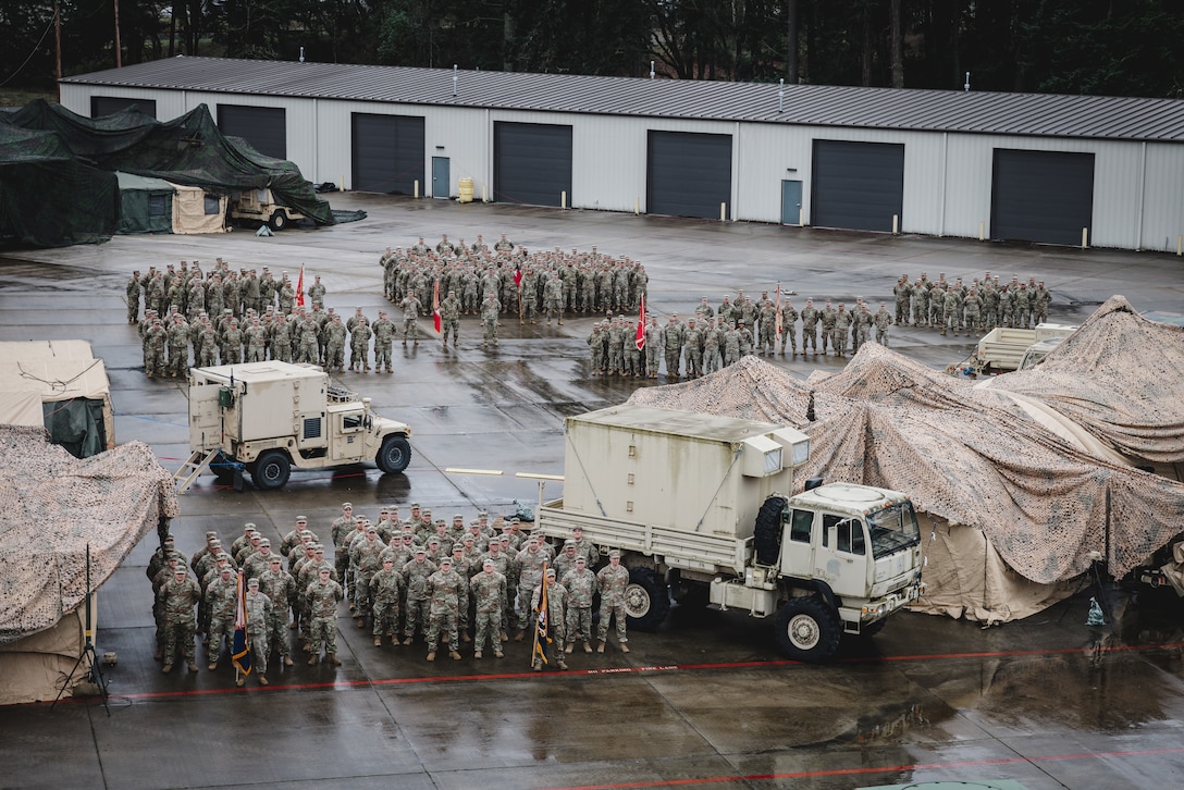 Soldiers stand in groups near trucks and covered equipment outside after rainfall.