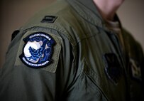 A black, blue and white heritage patch, worn on the shoulder of a man in green military uniform, displays a wolf howling at a moon.