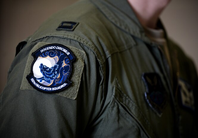 A black, blue and white heritage patch, worn on the shoulder of a man in green military uniform, displays a wolf howling at a moon.