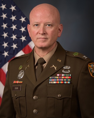 Photo of a service member in uniform with the U.S. flag behind.