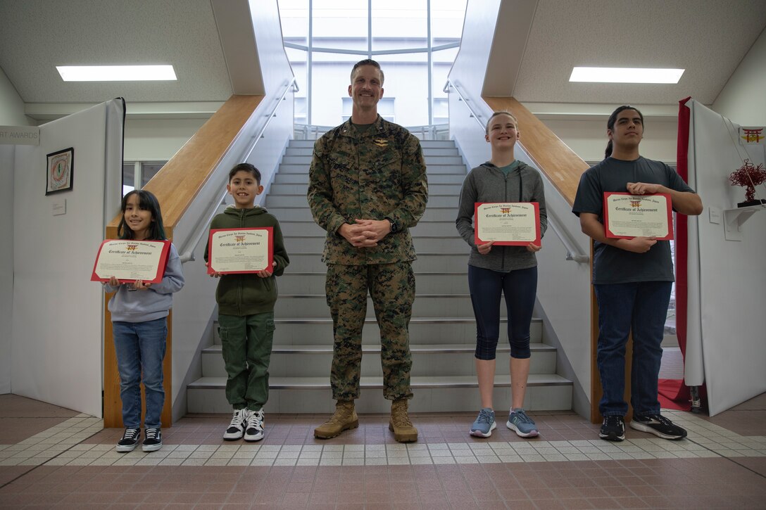 U.S. Marine Corps Lt. Col. Paul Cordes, center, the commanding officer of Marine Corps Air Station Iwakuni, poses for a group photo with the winners of the February 2024 MCAS Iwakuni Art Awards at MCAS Iwakuni, Japan, Feb. 22, 2024. The air station presented awards for its monthly art competition in which students attending schools at the air station showcase their artistic talent through different art mediums. (U.S. Marine Corps photo by Lance Cpl. Dahkareo Pritchett)