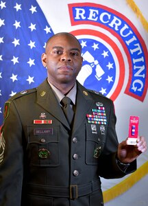 man wearing u.s. army uniform standing in front of flags holds a ribbon in his left hand.