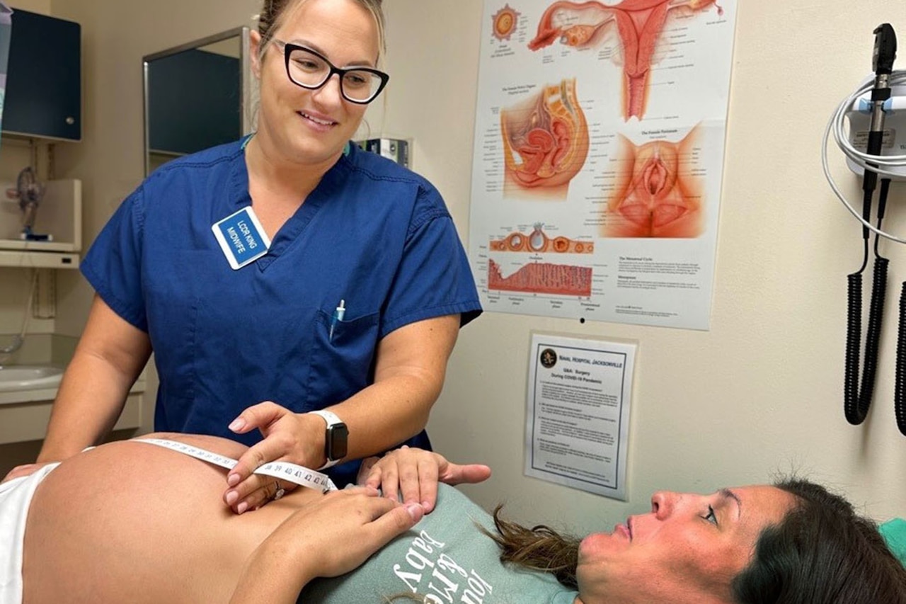 A nurse in medical scrubs measures a pregnant woman’s belly.