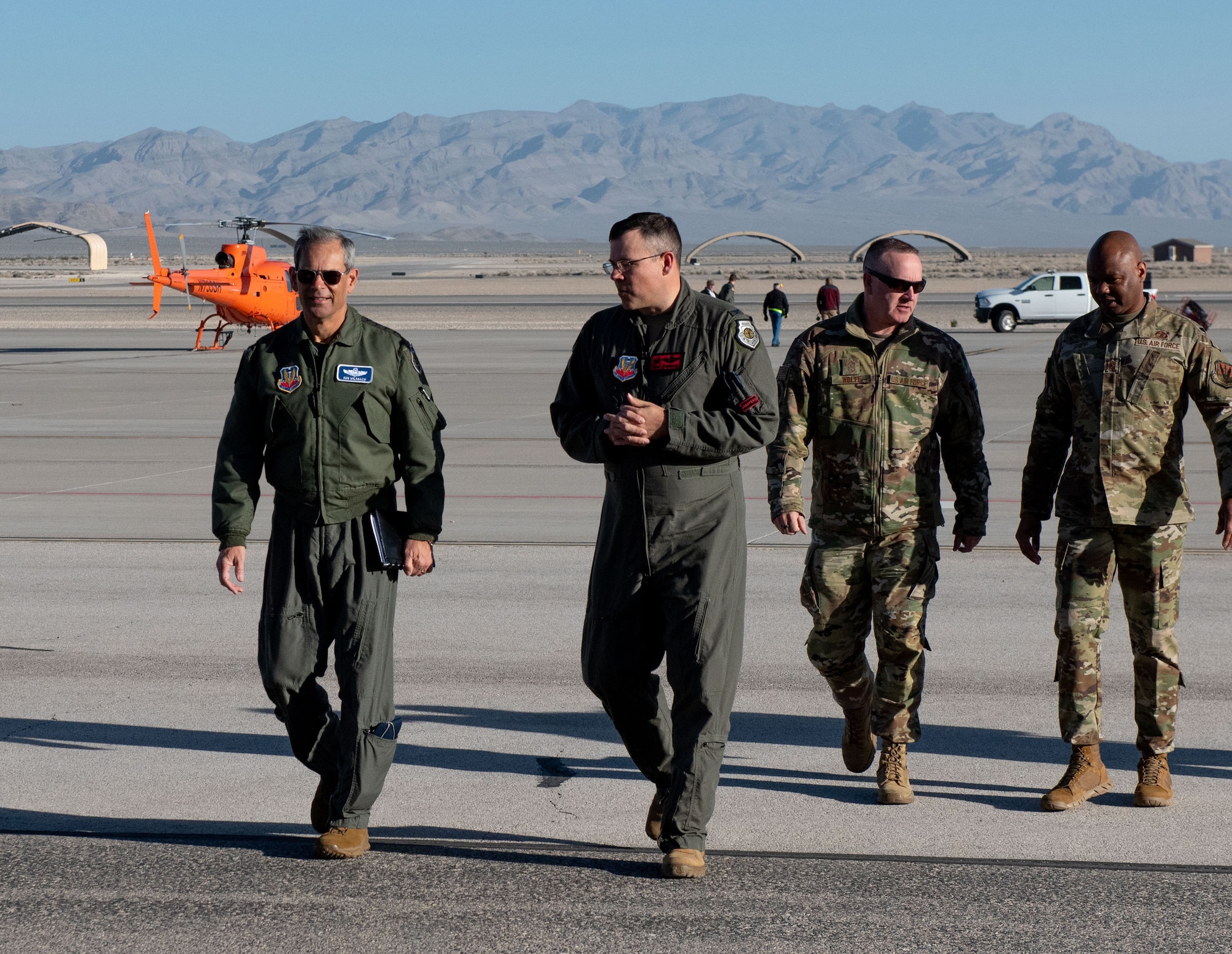 Four airmen walk on the flightline away from an orange helicopter.