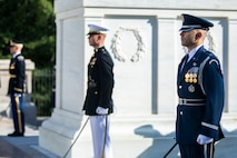 Three service members are flanking the Tomb of the Unknown Soldier. They each have a sword in their hand that is pointing toward the ground.