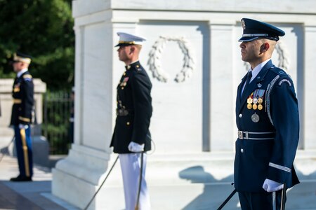 Three service members are flanking the Tomb of the Unknown Soldier. They each have a sword in their hand that is pointing toward the ground.