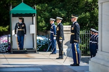 Service members stand near the Tomb of the Unknown Soldier with swords in hand pointed toward the ground. Another Soldier is standing inside a small green tent.