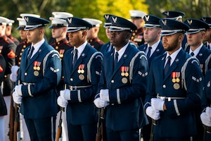 Members of the US Air Force Honor Guard are standing at rest with their ceremonial rifles in front of them with the butt of the rifle on the ground. They are dressed in Air Force blue uniforms