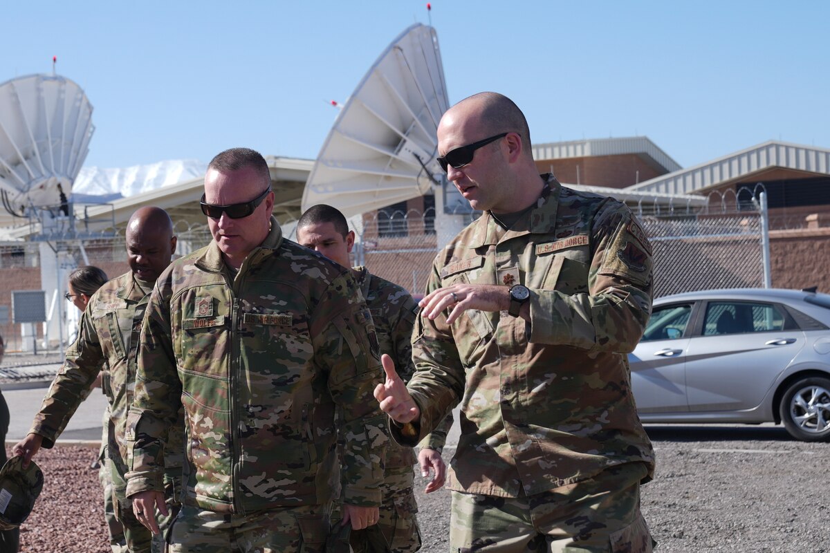 Airmen walk while one explains the satellites which are in the background to another airmen.