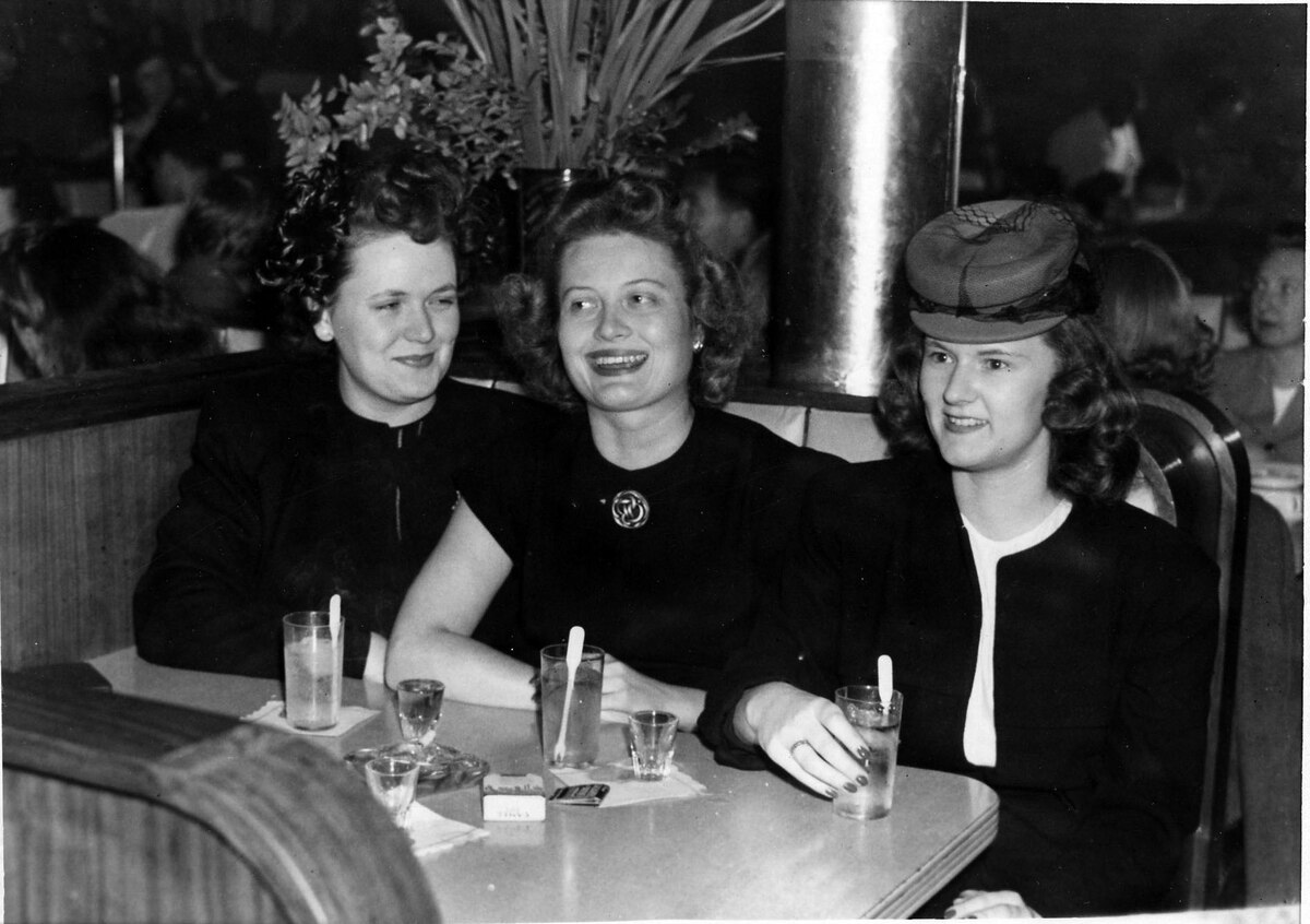 three women sit at a booth in a restaurant in a black and white image