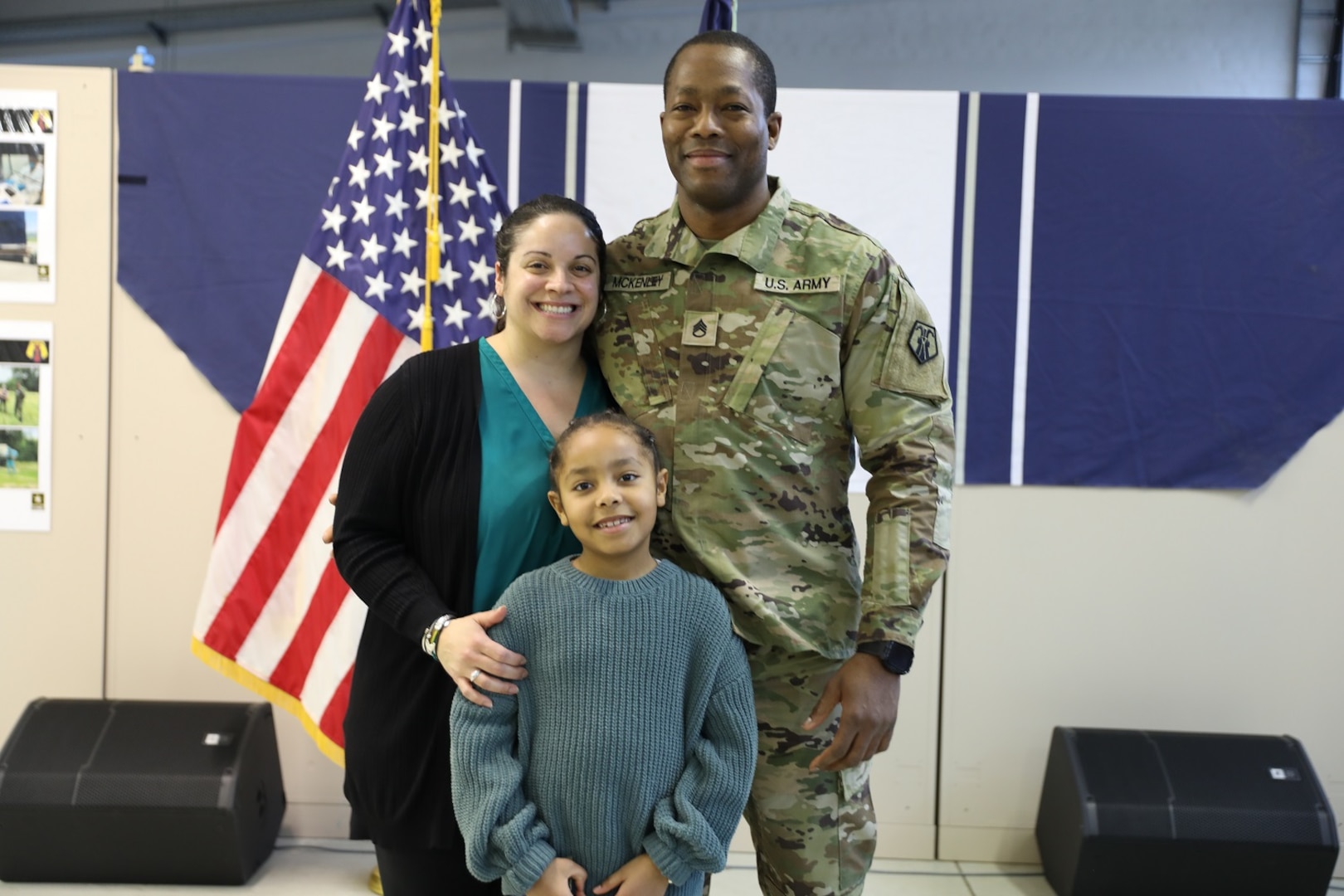 Uniformed service member smiles and stands with wife and daughter at promotion ceremony.