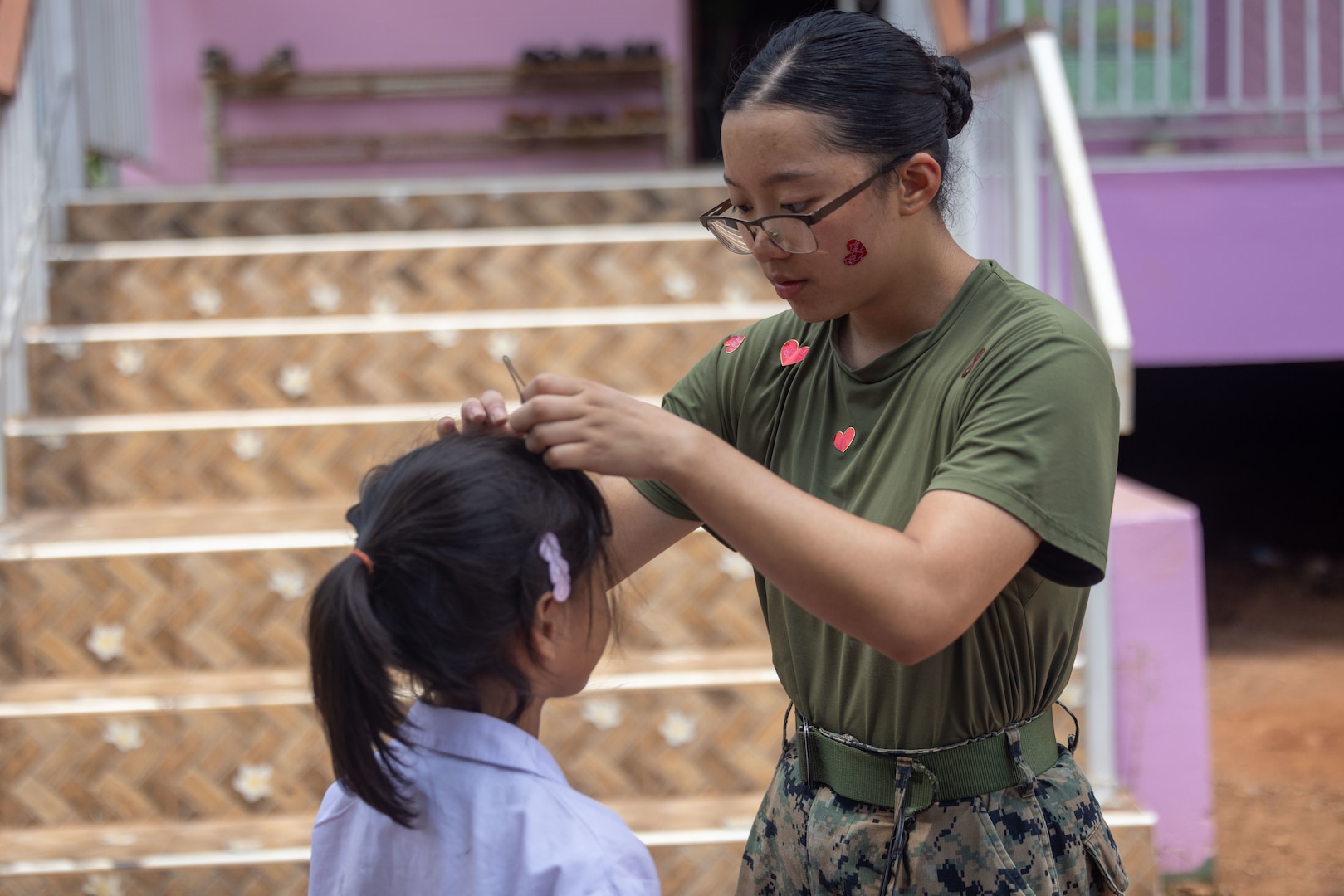 U.S. Marine Corps Cpl. Katie Lee, a supply chain and materiel management specialist with Marine Wing Support Squadron (MWSS) 171, Marine Aircraft Group 12, and native of New York, fixes the hair of a student from the Ban Prakaet School at Chanthaburi, Thailand, Feb. 21, 2024. Marines of MWSS-171 lent their engineering expertise to multilateral humanitarian efforts during Cobra Gold 24. Joint Exercise Cobra Gold is the largest joint exercise in mainland Asia and a concrete example of the strong alliance and strategic relationship between Thailand and the United States.  This is the 43rd iteration of the multilateral exercise held from Feb. 27 to March 8, 2024. (U.S. Marine Corps Photo by Cpl. Calah Thompson)