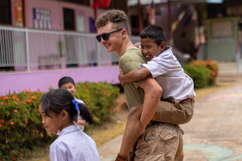 U.S. Marine Corps Lance Cpl. Kyle Bedrosian, a combat engineer with Marine Wing Support Squadron (MWSS) 171, Marine Aircraft Group 12, and a native of California, carries a student on his back at the Ban Prakaet School in Chanthaburi, Thailand, Feb. 29, 2024. Marines of MWSS-171 lent their engineering expertise to multilateral humanitarian efforts during Cobra Gold 24. Joint Exercise Cobra Gold is the largest joint exercise in mainland Asia and a concrete example of the strong alliance and strategic relationship between Thailand and the United States. This year will be the 43rd iteration of the multilateral exercise and will be held from Feb. 27 to March 8, 2024. (U.S. Marine Corps photo by Cpl. Calah Thompson)