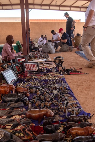 Handmade items for sale are laid out on the ground as people speak with vendors in the background.
