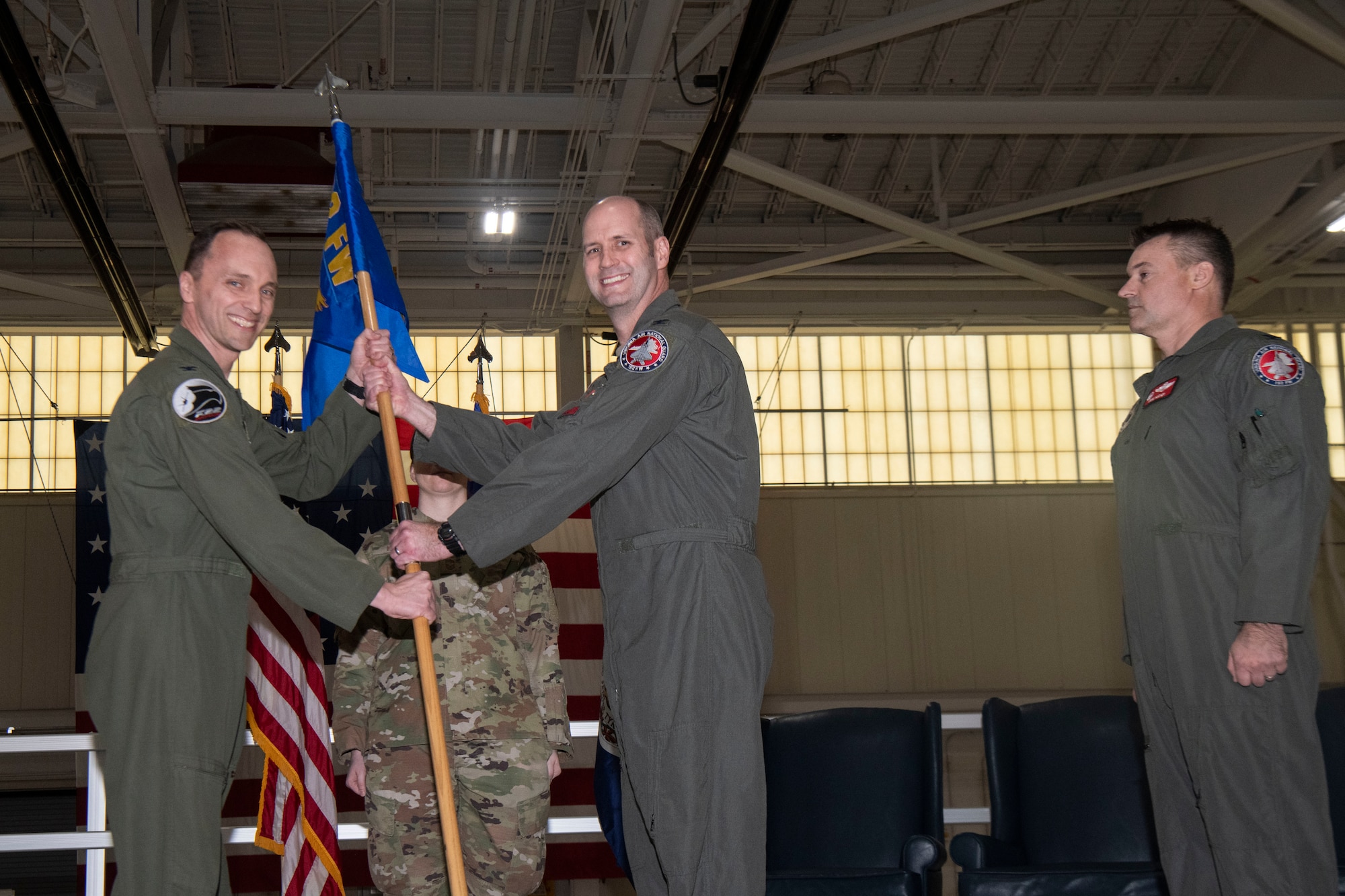 3 Air Force officers standing on stage, 2 holding a guidon