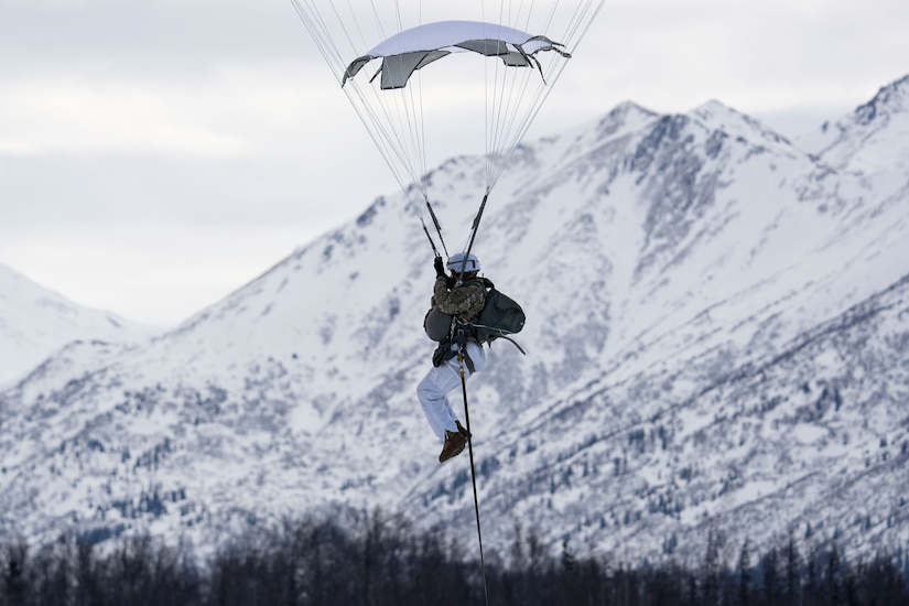 An Army paratrooper prepares to land after jumping from a military aircraft on a gray, cloudy day.