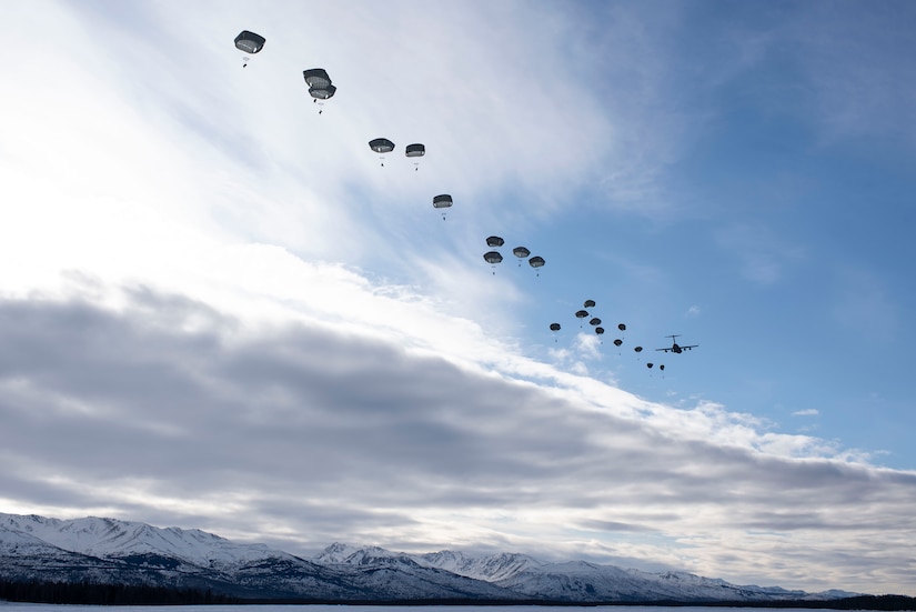Paratroopers jump from a military aircraft on a cloudy day.