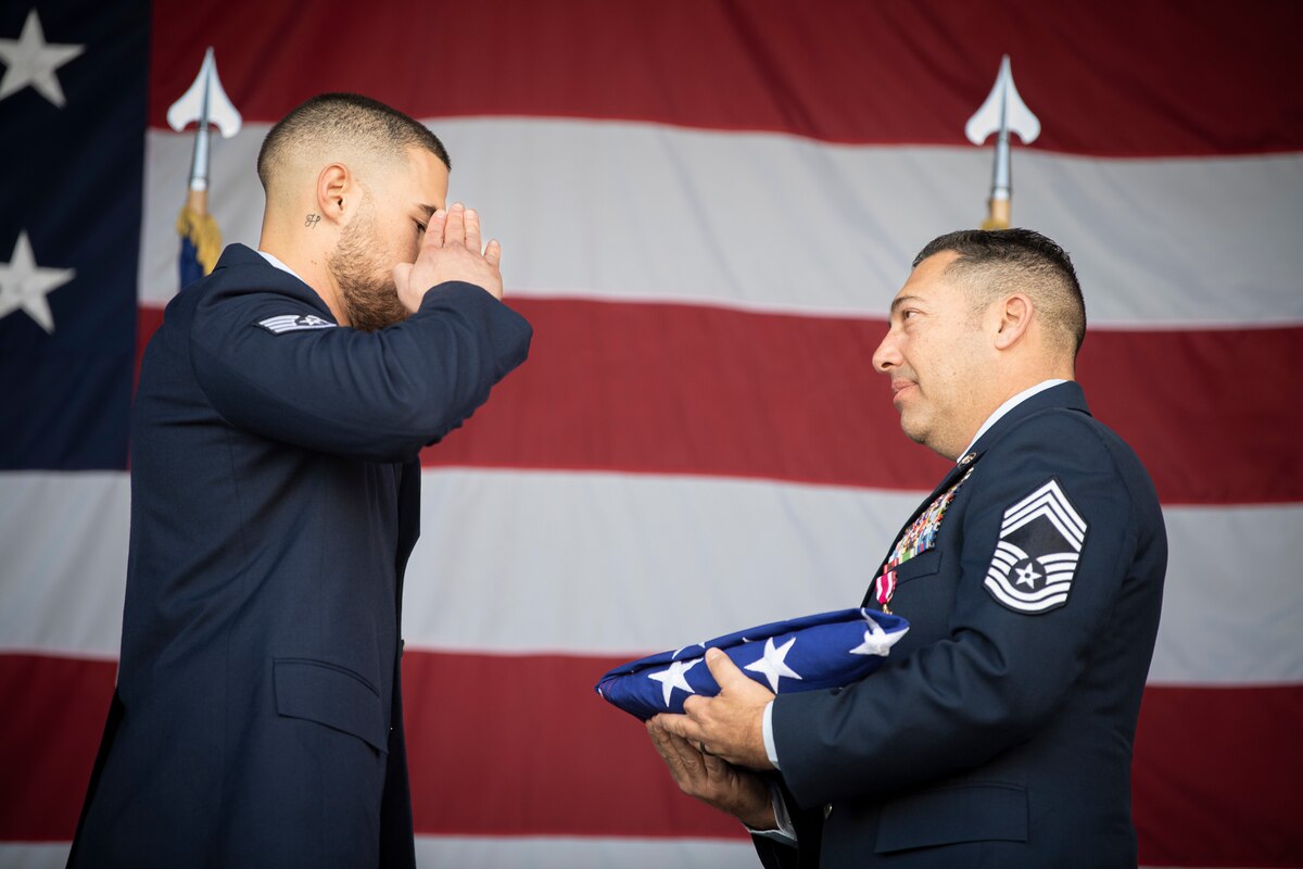 U.S. Air Force Staff Sgt. Elijah De La Torre, 821st Contingency Response Squadron executive assistant, salutes the flag for retired Chief Master Sgt. Paul Valenzuela, right, former 821st CRS senior enlisted leader, during Valenzuela's retirement ceremony at Hangar 818 on Travis Air Force Base, Calif., March 8, 2024.