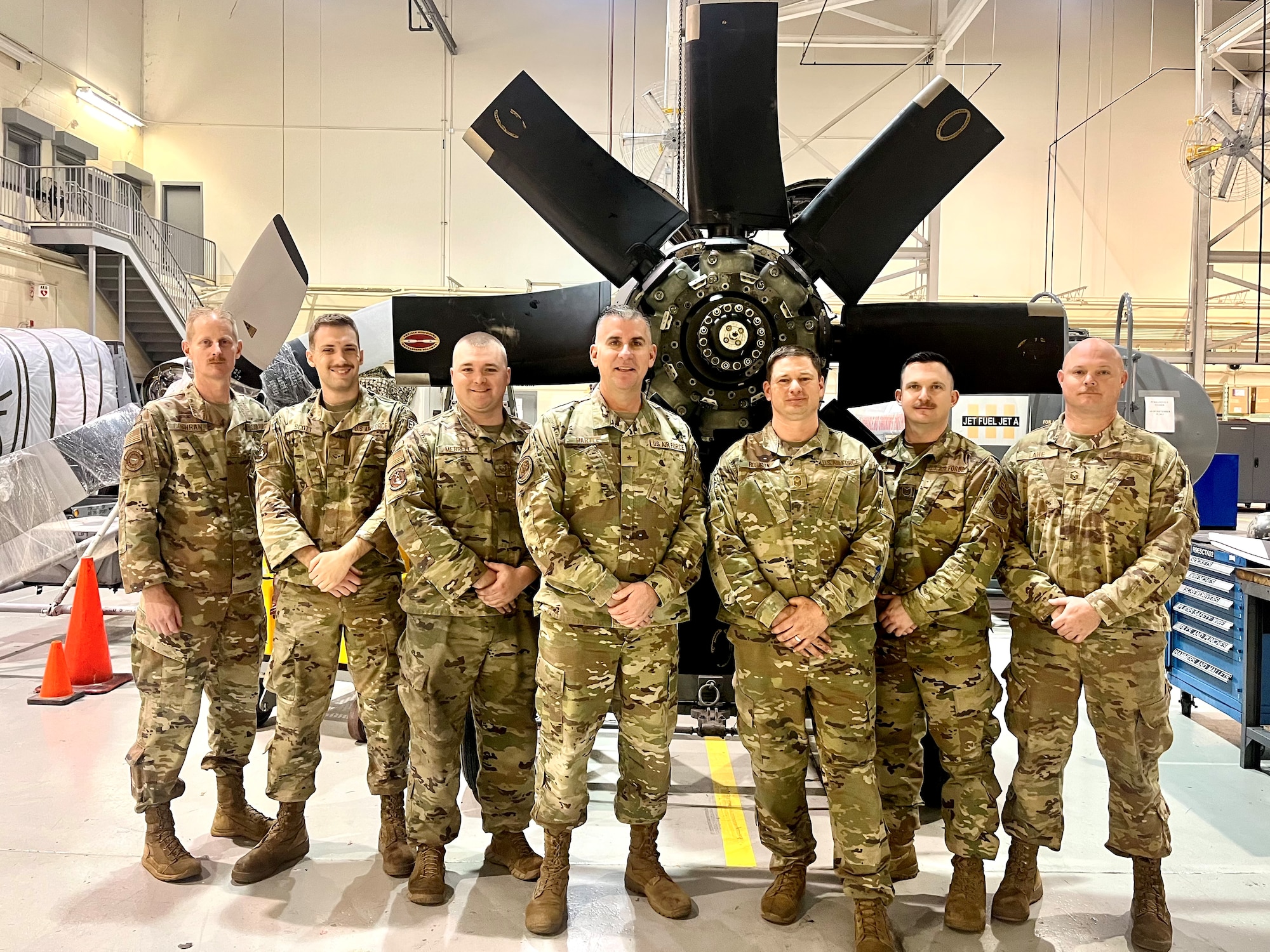 a group of people in military uniforms stands in front of an aircraft propeller