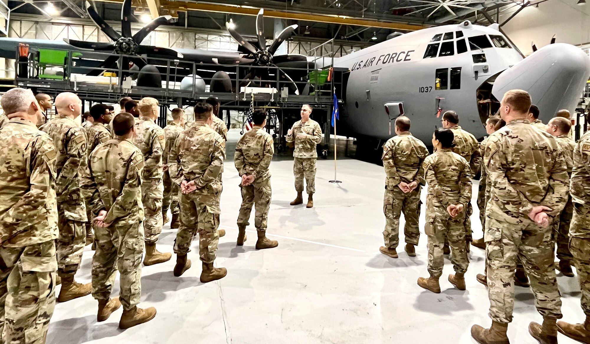 a man in a military uniform stands in front of an airplane and speaks to a group of people in military uniforms