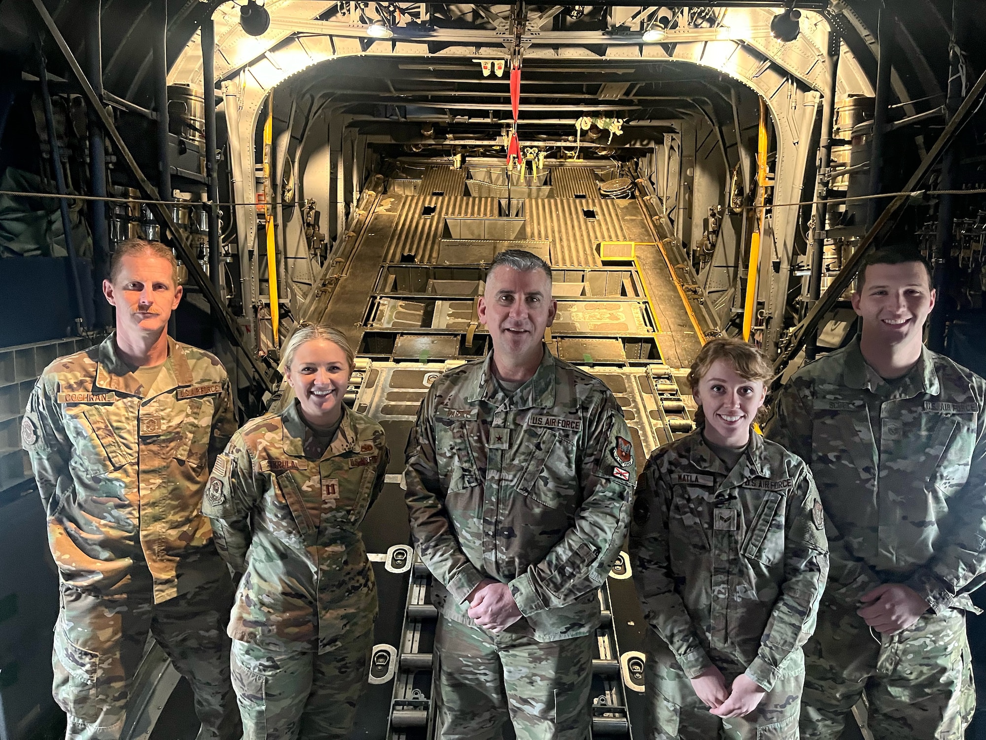 a group of people in military uniforms stand in front of an aircraft with its rear cargo ramp open