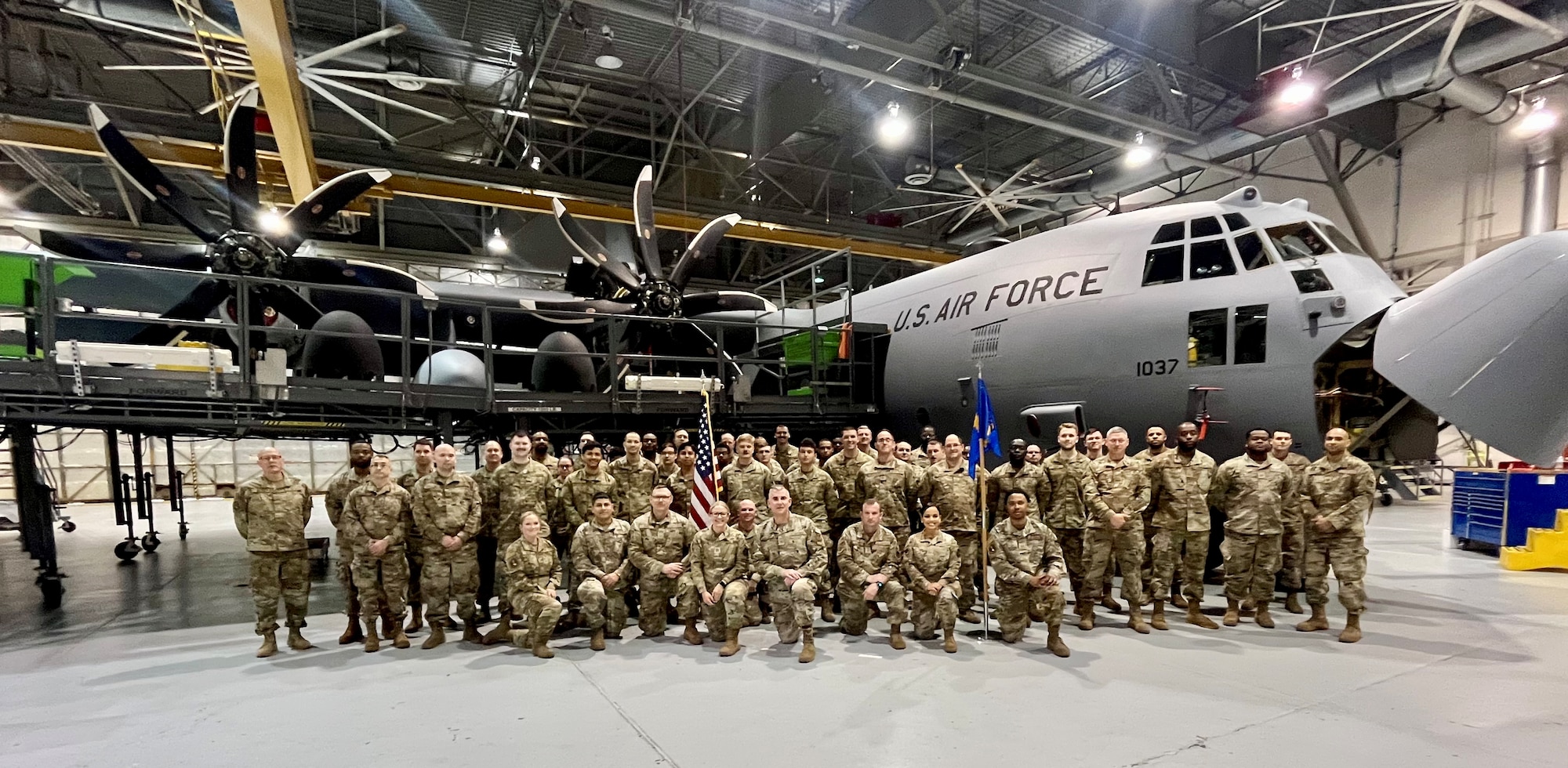 a group of people in military uniforms stands in front of an airplane inside of a hangar