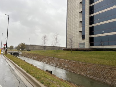 A flooded stream flows in a straight concrete basin through built structures.
