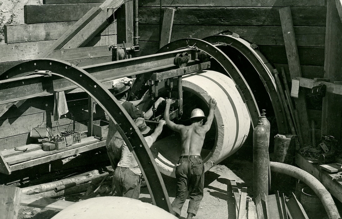 Three men push a large concrete cylinder into place.