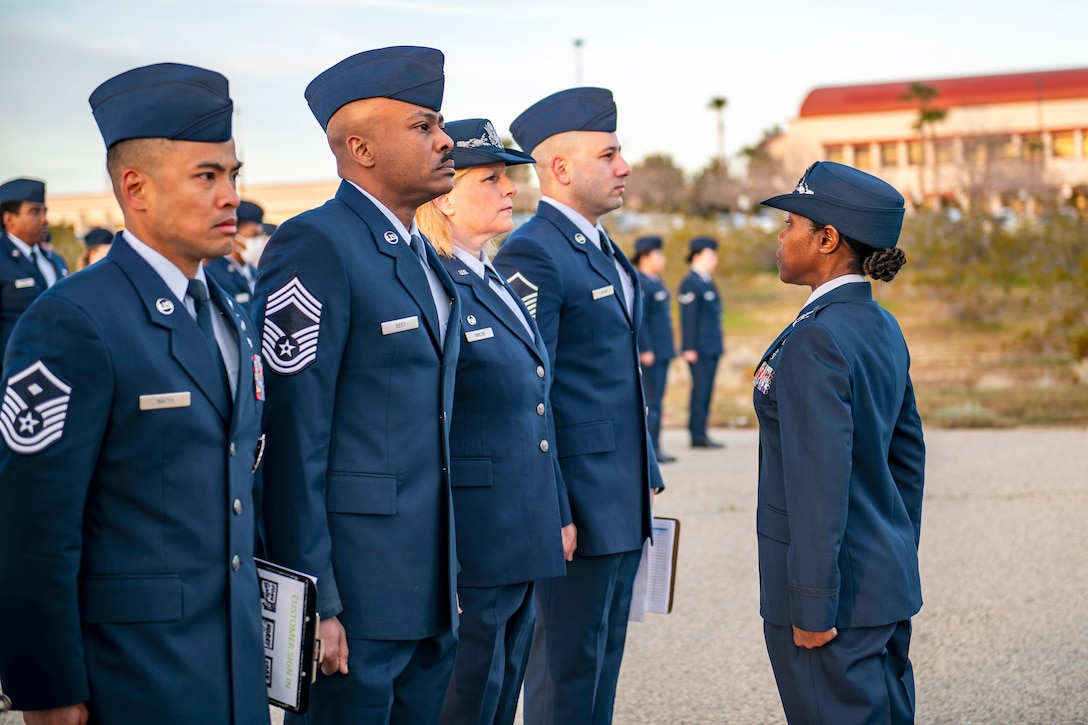 An airman standing at attention faces four airmen standing in formation with grass and a building in the background.