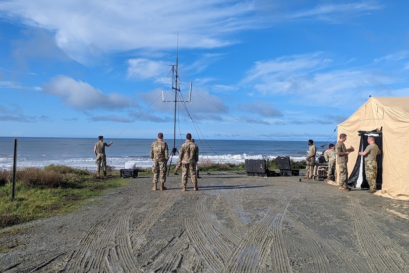 Uniformed service members set up a camp on a beach.