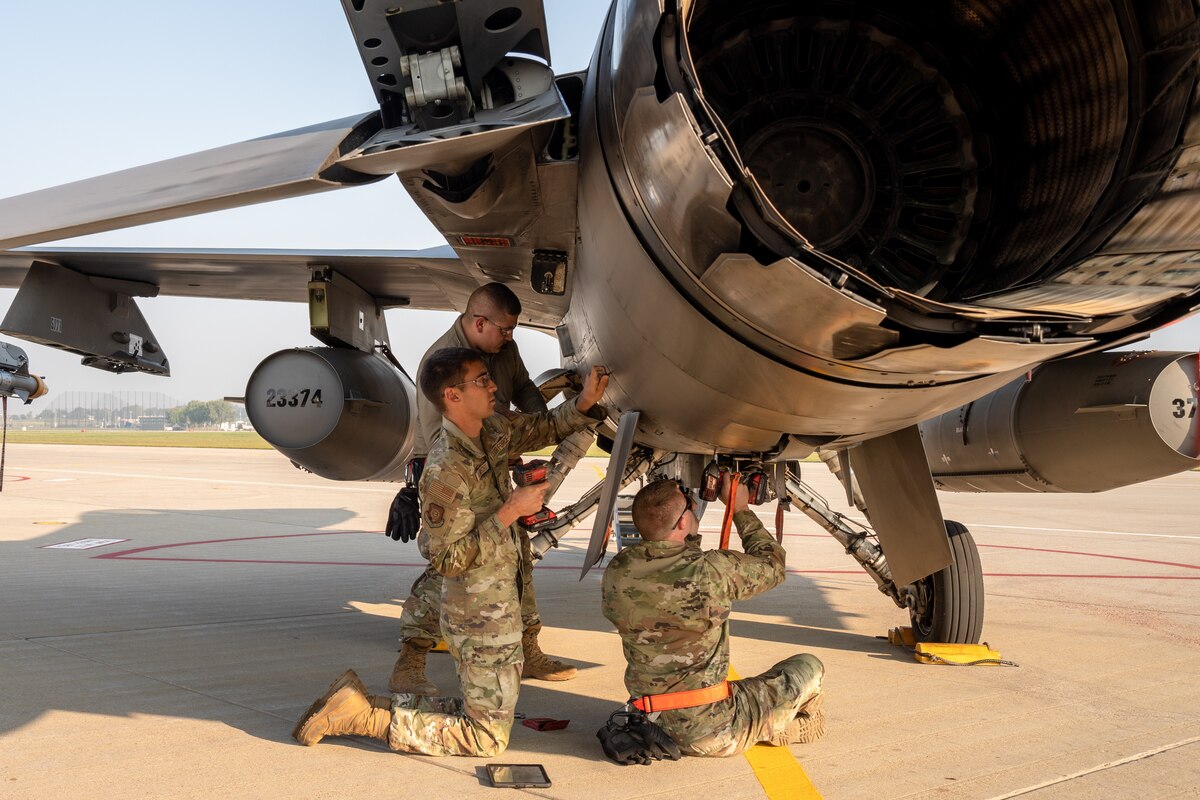 Several uniformed service members perform maintenance on a military aircraft.