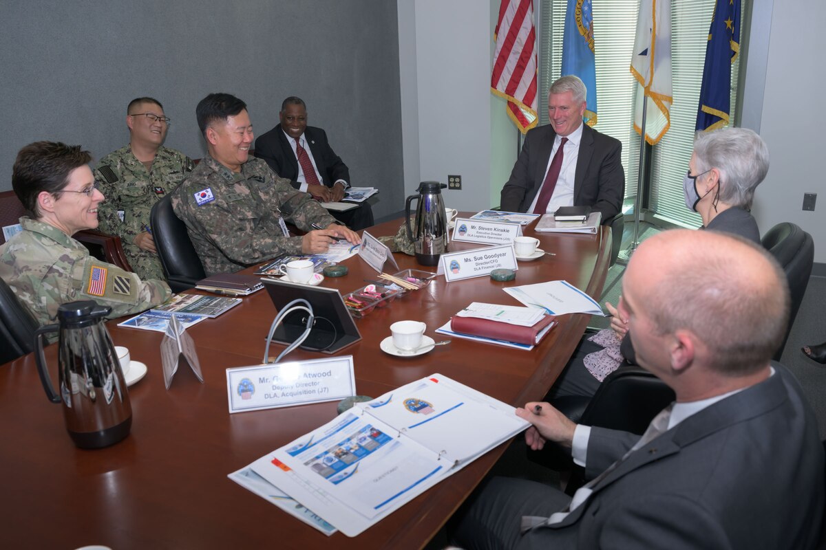 Several civilians and uniformed military members sit at a table while smiling.