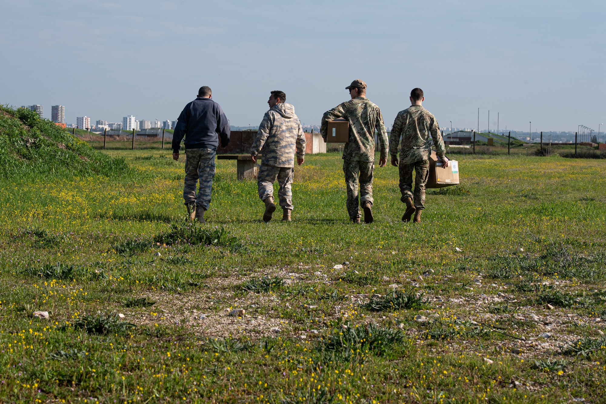 Two Turkish and two U.S. Air Force explosive ordnance disposal team members walk with supplies to dispose of unserviceable munitions towards the disposal site.