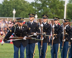 Army Soldiers in dark ceremonial uniforms are standing in a line doing various movements with their rifles.